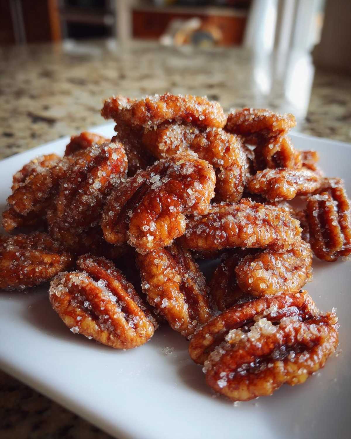 A pile of glistening, caramelized cinnamon sugar pecans heavily coated in visible sugar crystals, served on a white plate.