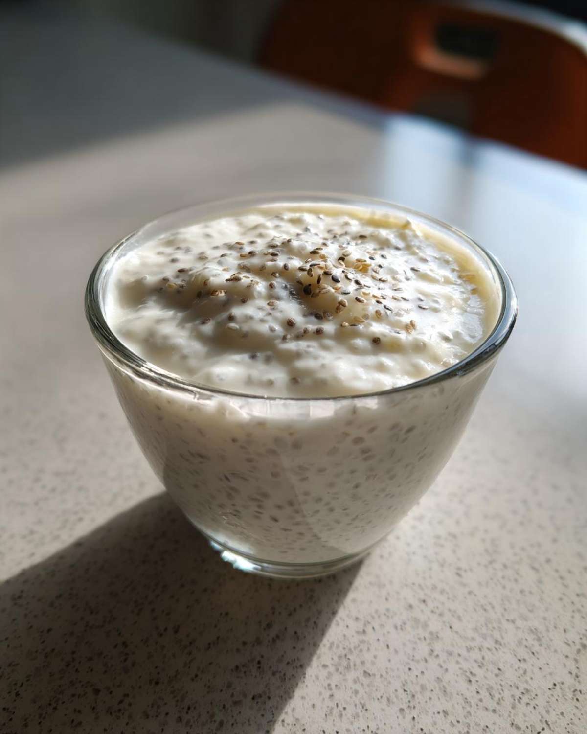 A glass filled with creamy white coconut chia pudding, topped with extra chia seeds.