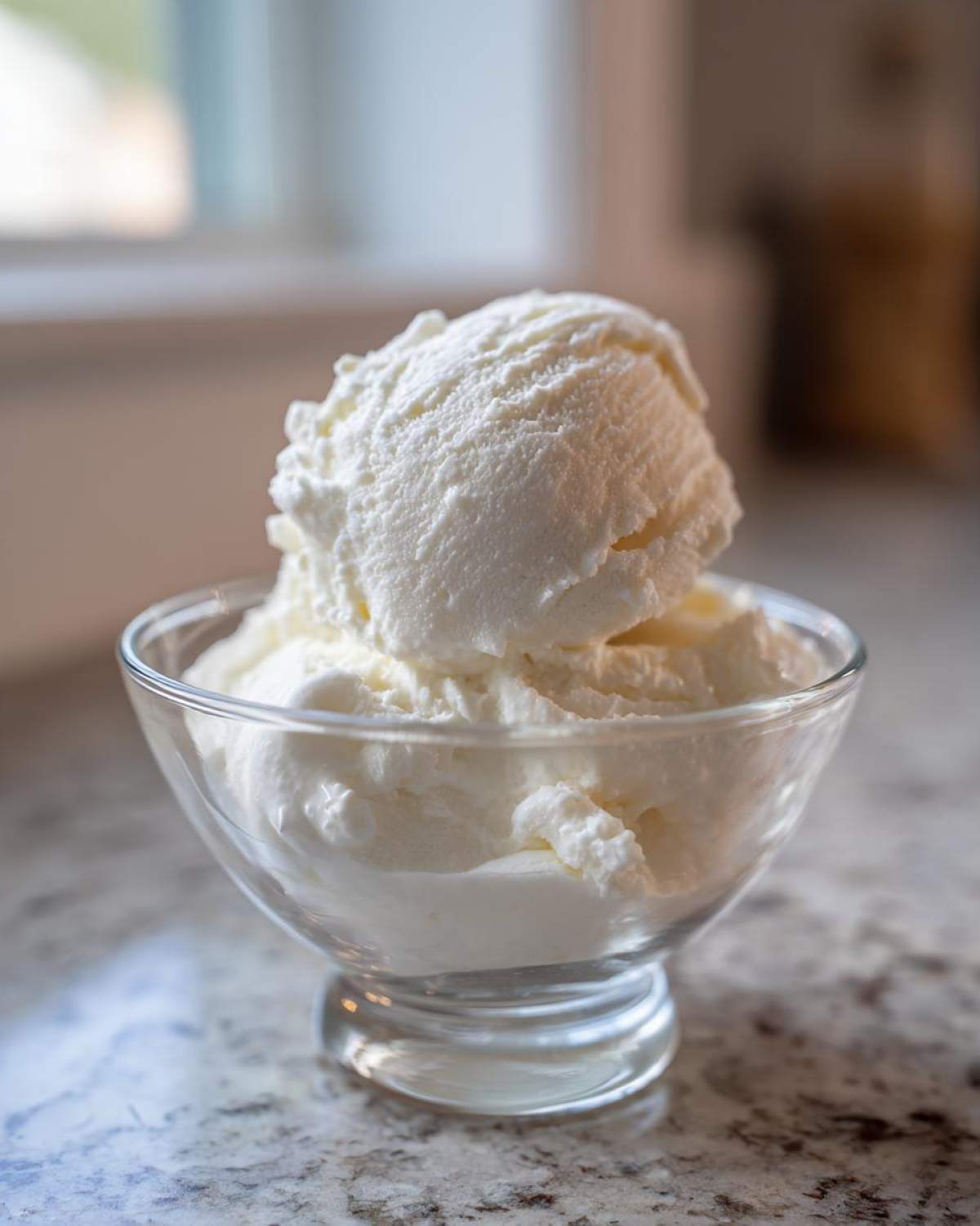 A close-up of a generous scoop of white, creamy cottage cheese ice cream served in a clear glass dessert dish.