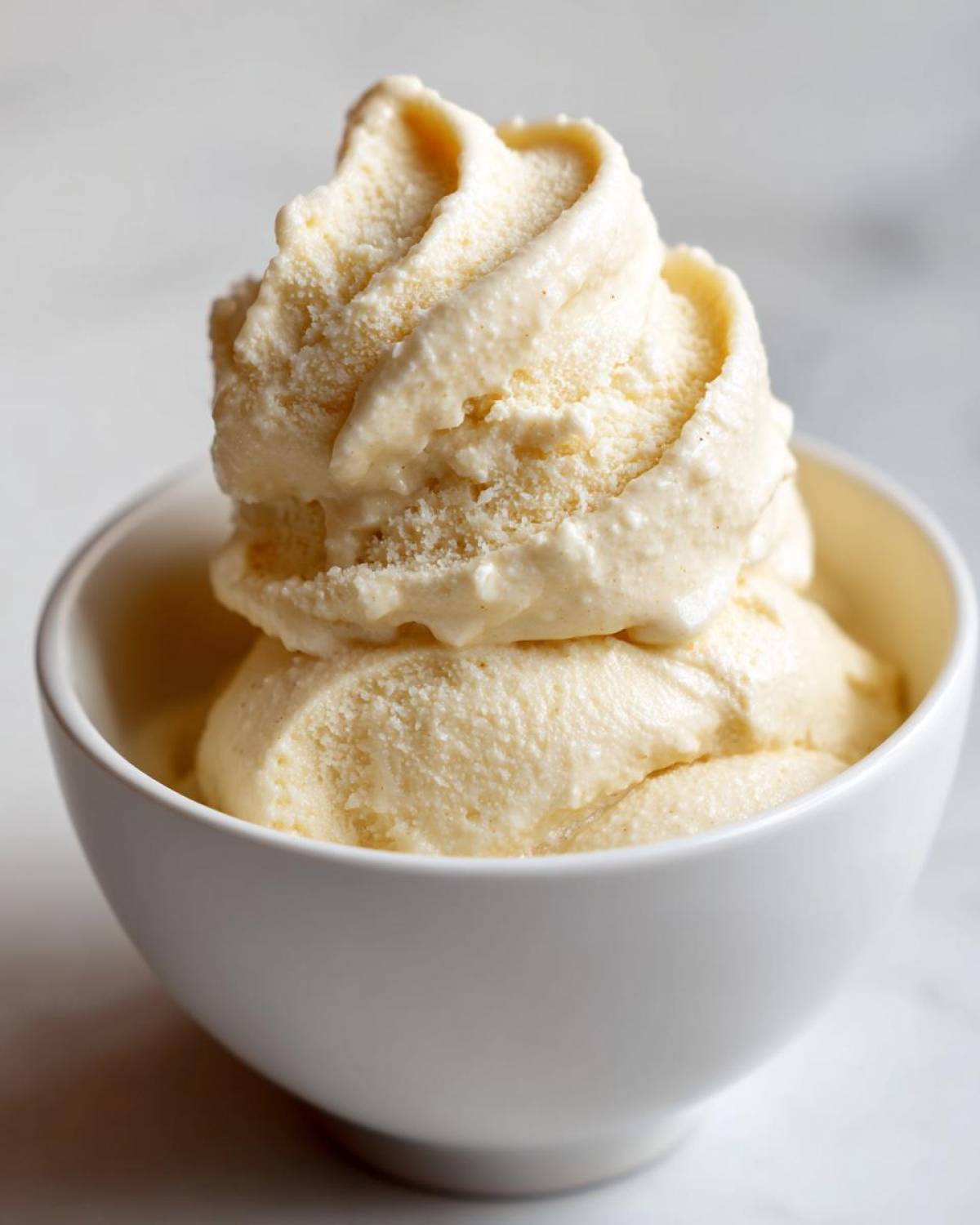 A close-up of creamy, soft-serve style banana ice cream swirled high in a small white bowl.