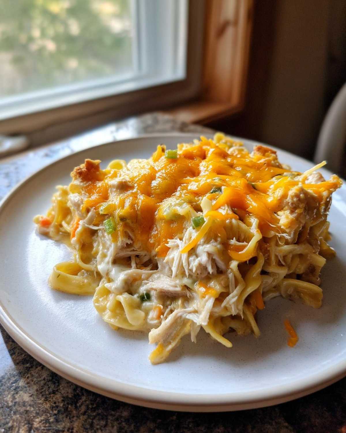 A generous serving of creamy chicken noodle casserole topped with melted cheddar cheese and green onions.
