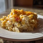 A close-up serving of creamy chicken noodle casserole topped with melted cheddar cheese on a white plate.