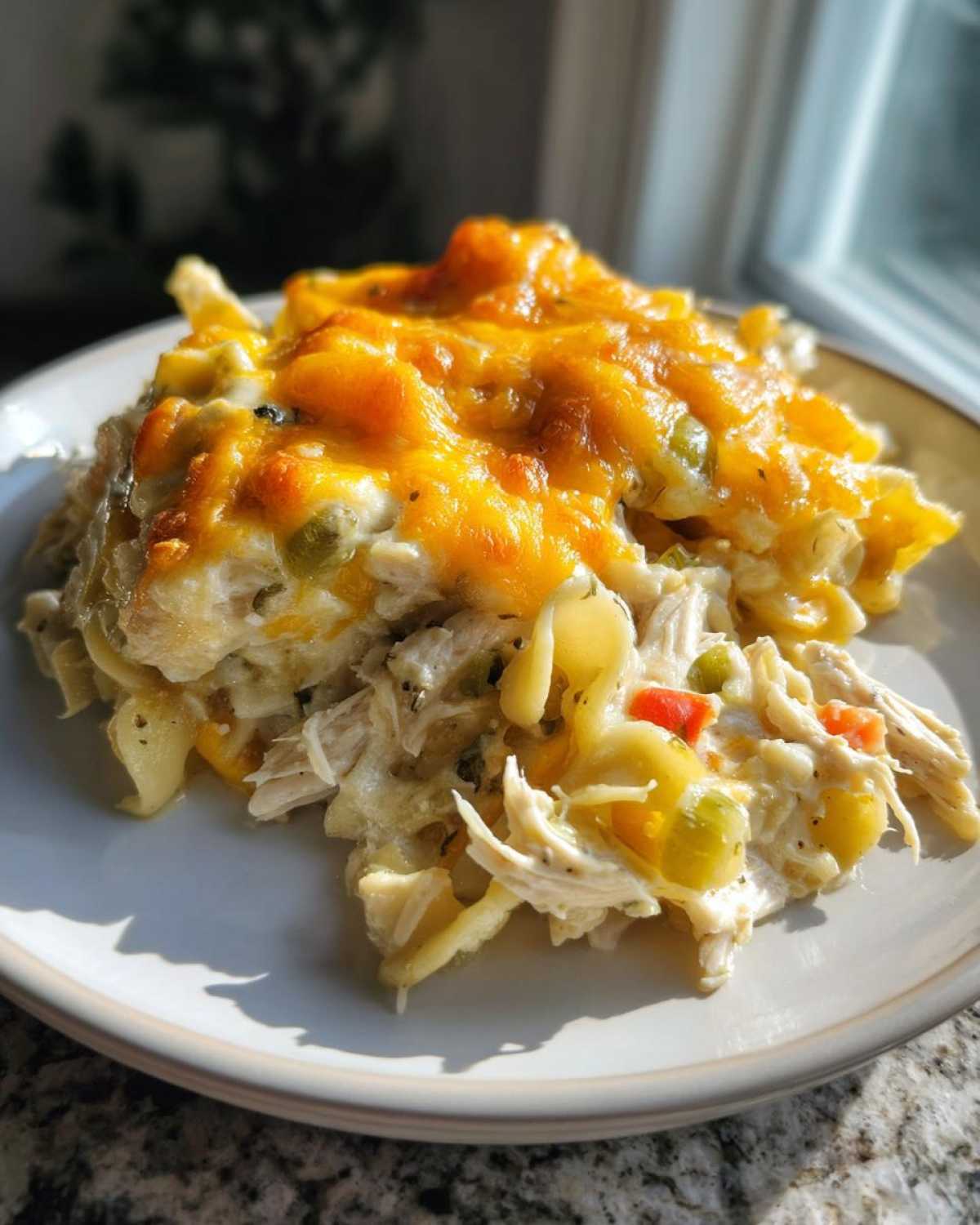 A close-up serving of creamy chicken noodle casserole topped with melted, golden cheddar cheese.