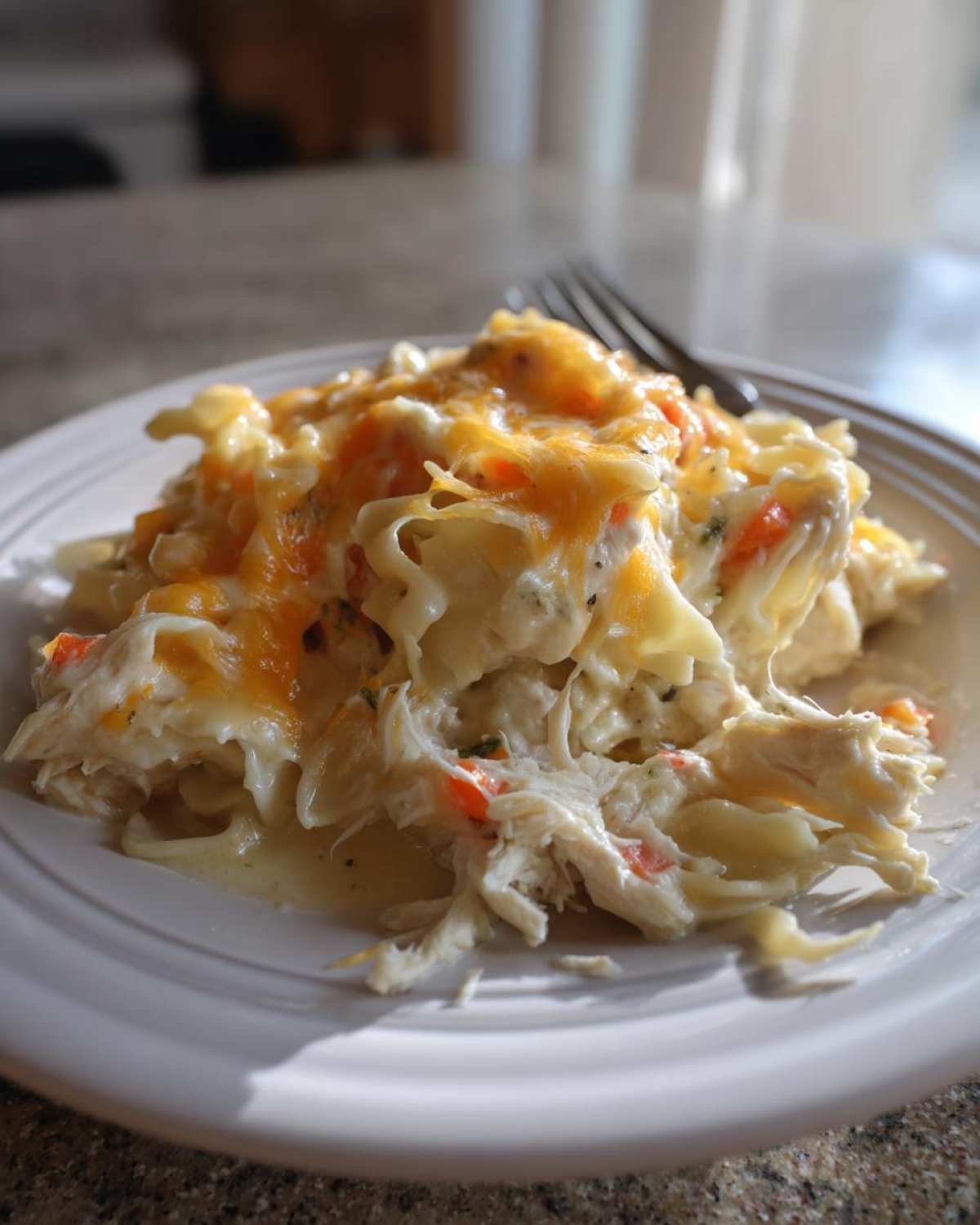 A serving of creamy chicken noodle casserole topped with melted cheddar cheese on a white plate.