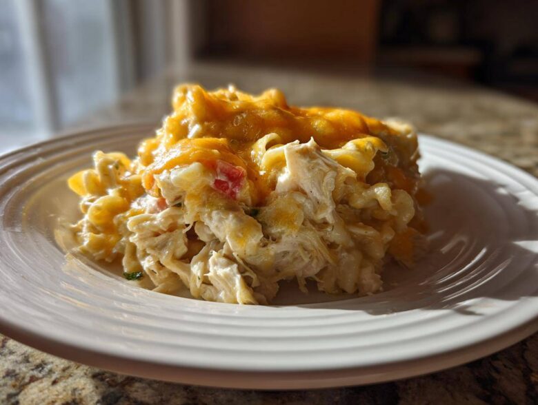 A close-up serving of creamy chicken noodle casserole topped with melted cheddar cheese on a white plate.