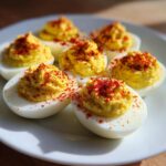 Close-up of six creamy classic deviled eggs piped high with filling and sprinkled generously with bright red paprika.