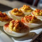 Six halves of classic deviled eggs filled with creamy yolk mixture and sprinkled with bright red paprika.