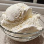 Close-up of several scoops of creamy white cottage cheese ice cream served in a clear glass bowl.