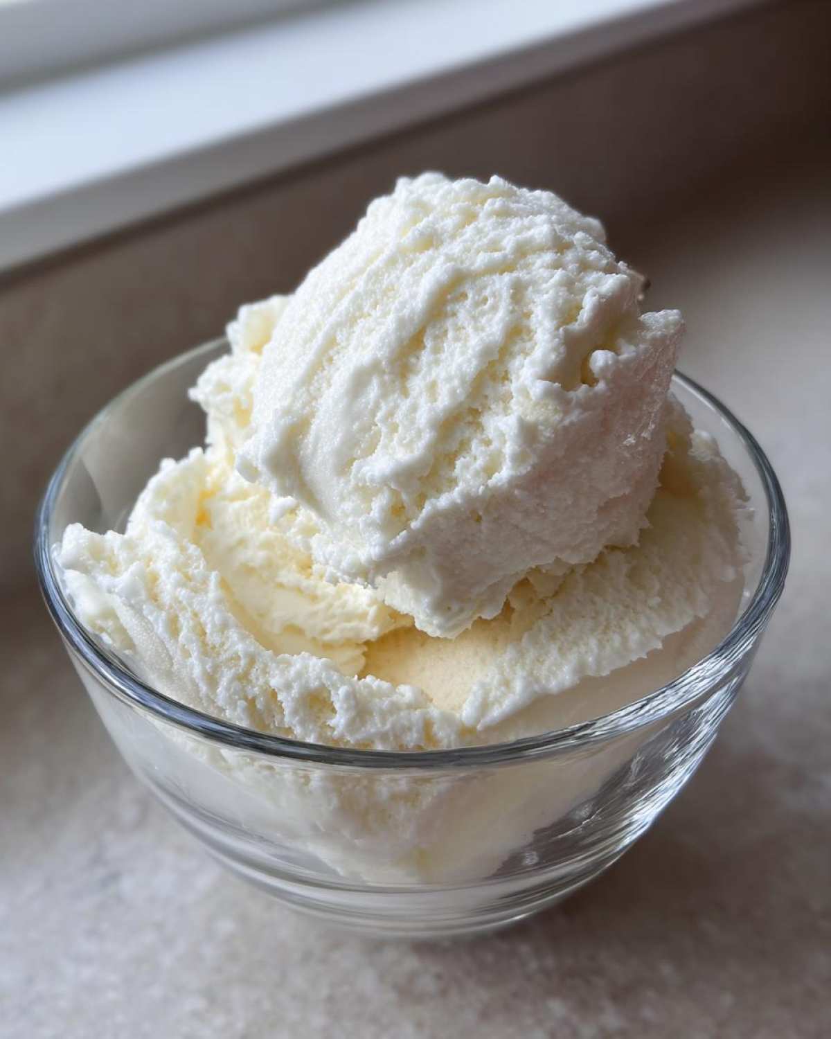 Two generous scoops of creamy, white cottage cheese ice cream served in a clear glass bowl.