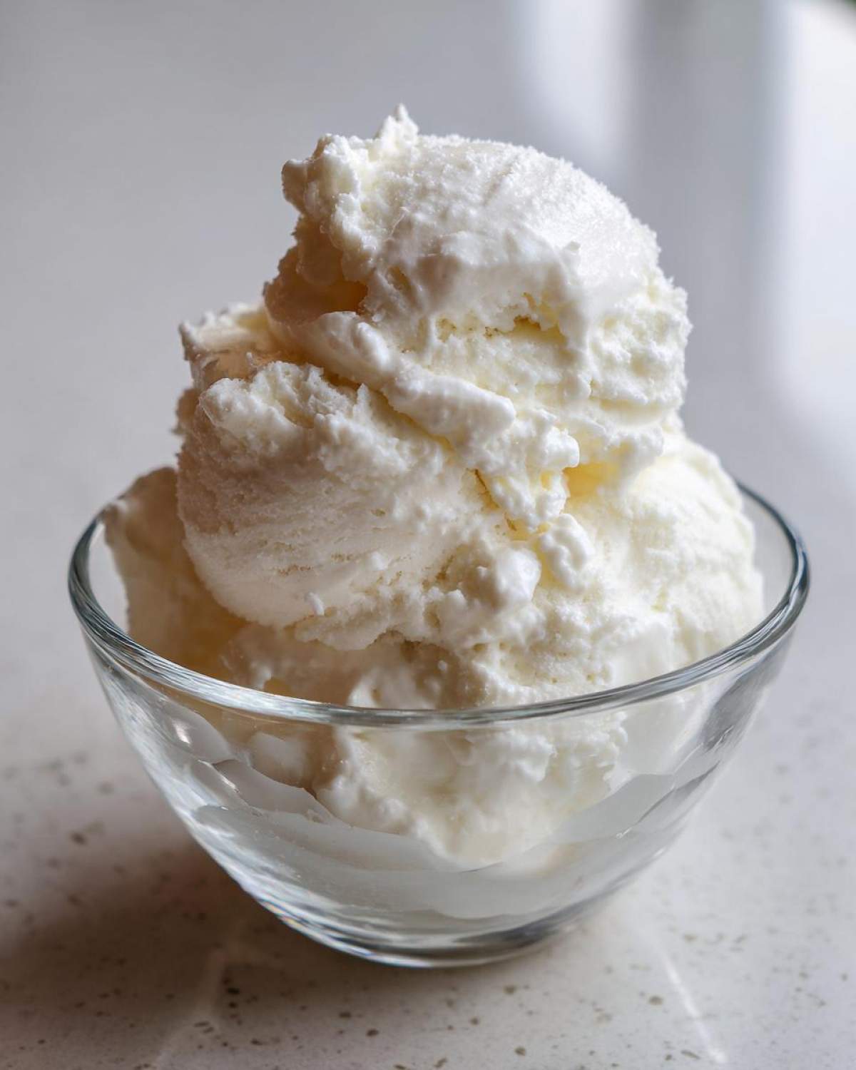 Two generous scoops of creamy white cottage cheese ice cream served in a small, clear glass bowl.