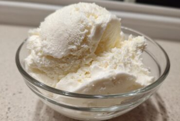 Close-up of several scoops of creamy white cottage cheese ice cream served in a clear glass bowl.