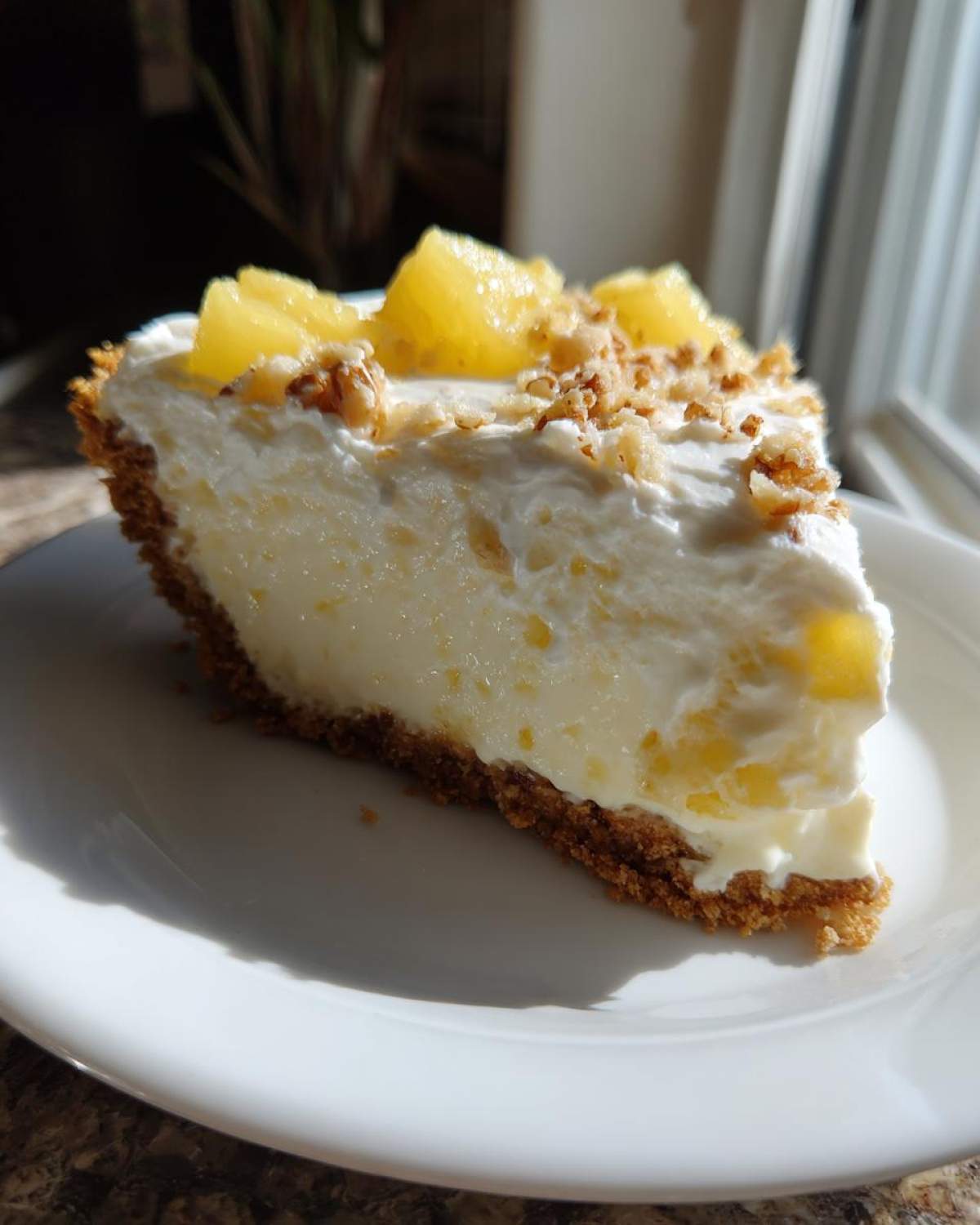 A generous slice of creamy million dollar pie with a graham cracker crust, topped with whipped cream, pineapple chunks, and chopped nuts.