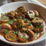 Close-up of whole button mushrooms smothered in a rich, brown creamy mushroom sauce and topped with fresh parsley.