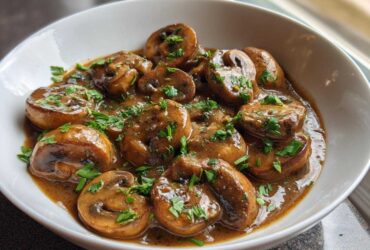 Close-up of whole button mushrooms smothered in a rich, brown creamy mushroom sauce and topped with fresh parsley.