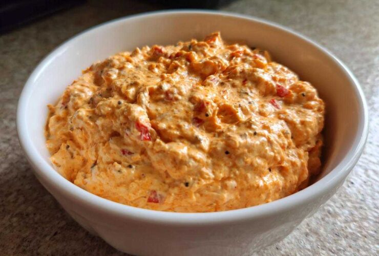 A close-up of creamy, orange-colored boat dip mixed with red pepper flakes and spices, served in a white bowl.