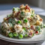 A close-up of a mound of creamy pea salad mixed with bacon bits and topped with crunchy crumbs.