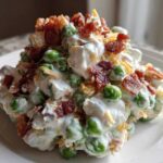 A scoop of creamy pea salad mixed with dressing, topped generously with crumbled bacon and shredded cheese.