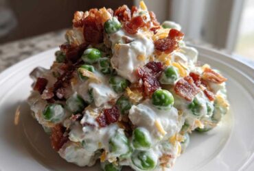 A scoop of creamy pea salad mixed with dressing, topped generously with crumbled bacon and shredded cheese.