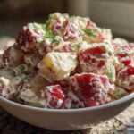 Close-up of a creamy red potato salad in a white bowl, garnished with fresh dill.