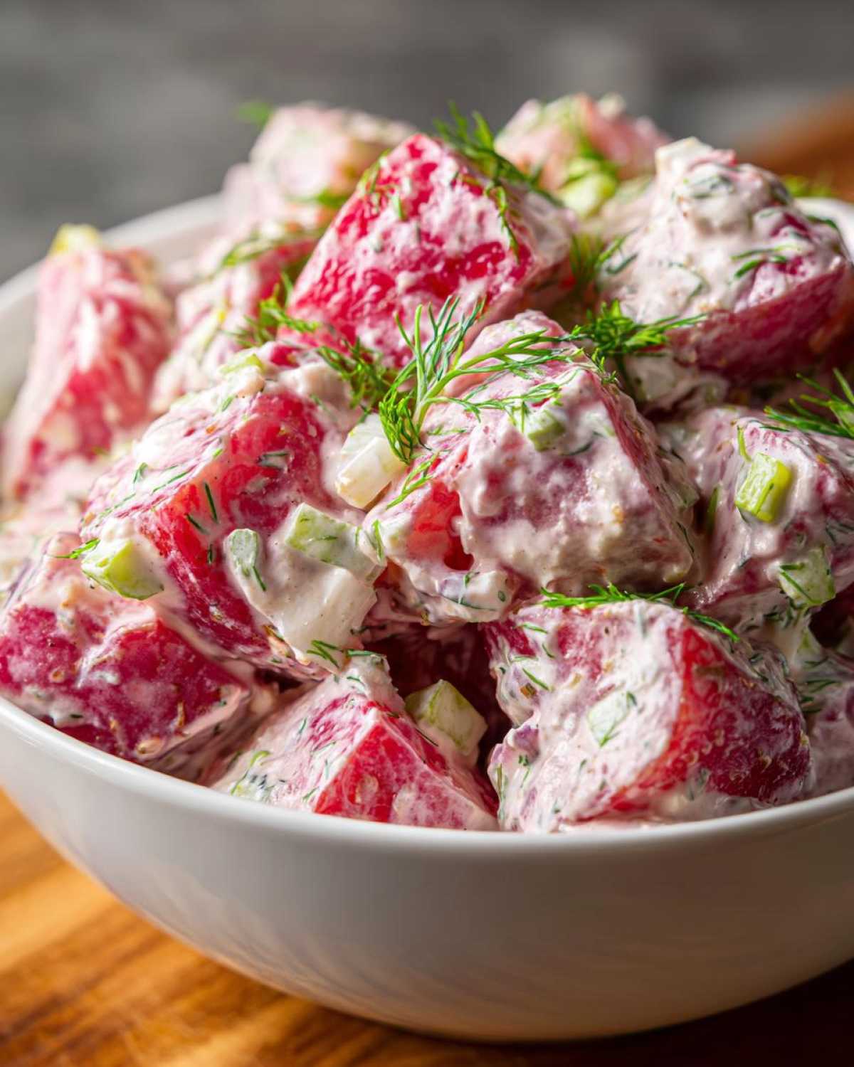 Close-up of creamy red potato salad chunks coated in dressing and garnished with fresh dill.