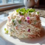 A molded serving of creamy seafood salad imitation crab topped with chopped green onions and red onion.