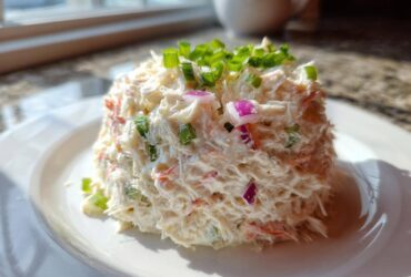 A molded serving of creamy seafood salad imitation crab topped with chopped green onions and red onion.