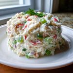 A mound of creamy seafood salad imitation crab mixed with diced green peppers and red onion, garnished with parsley.