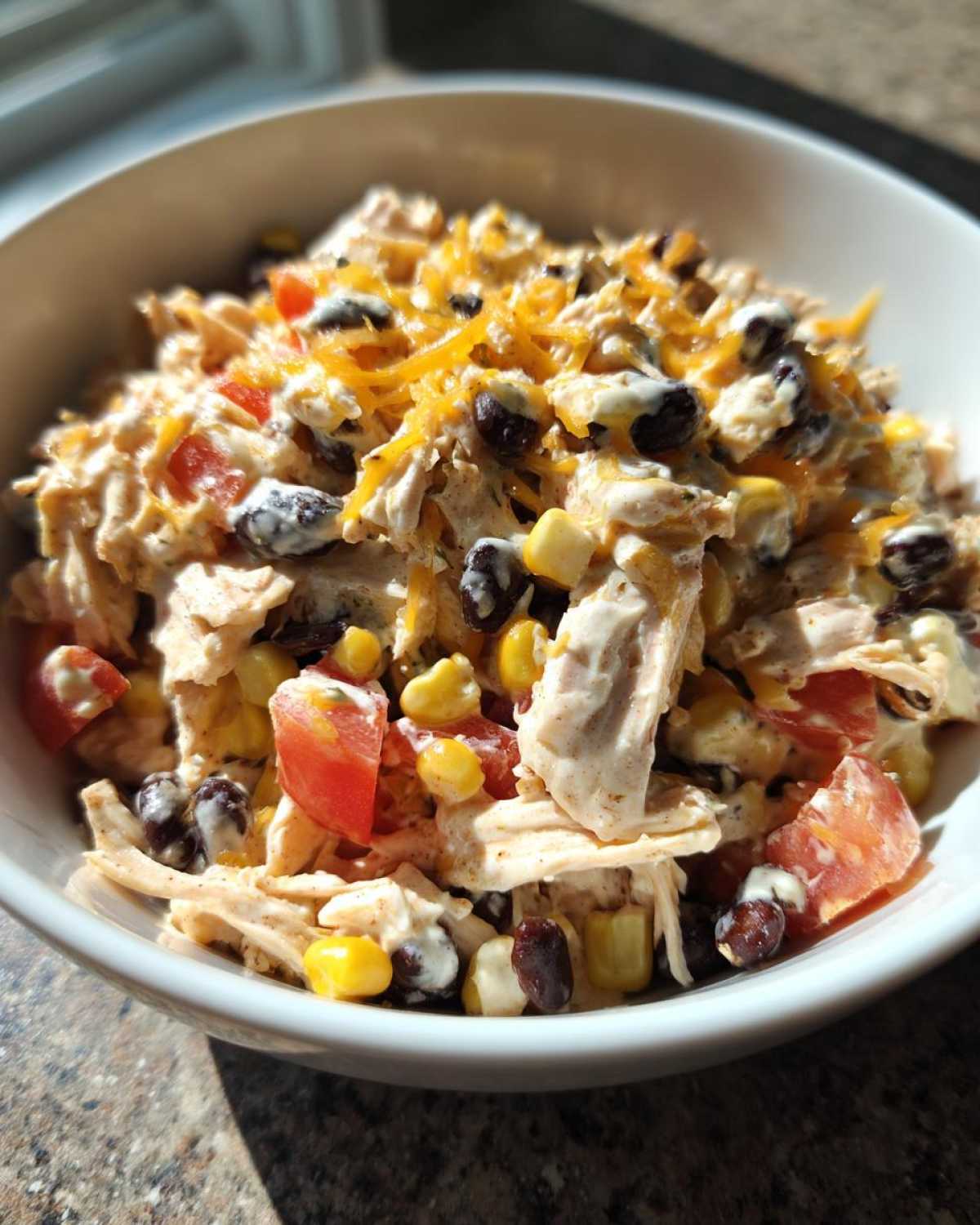 Close-up of a creamy southwest salad with shredded chicken, black beans, corn, tomatoes, and shredded cheese.
