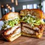 A thick, juicy Crispy Chicken Sandwich Dill Aioli cut in half, showing layers of fried chicken, pickles, and creamy sauce.