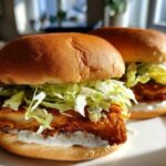 Two Crispy Chicken Sandwich Dill Aioli sandwiches featuring fried chicken, shredded lettuce, pickles, and creamy dill aioli on toasted buns.