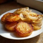 Close-up of perfectly golden brown, crispy fried potatoes served alongside soft, caramelized onion slices on a white plate.