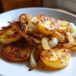 Close-up of golden brown, crispy fried potatoes mixed with soft, caramelized onions served on a white plate.