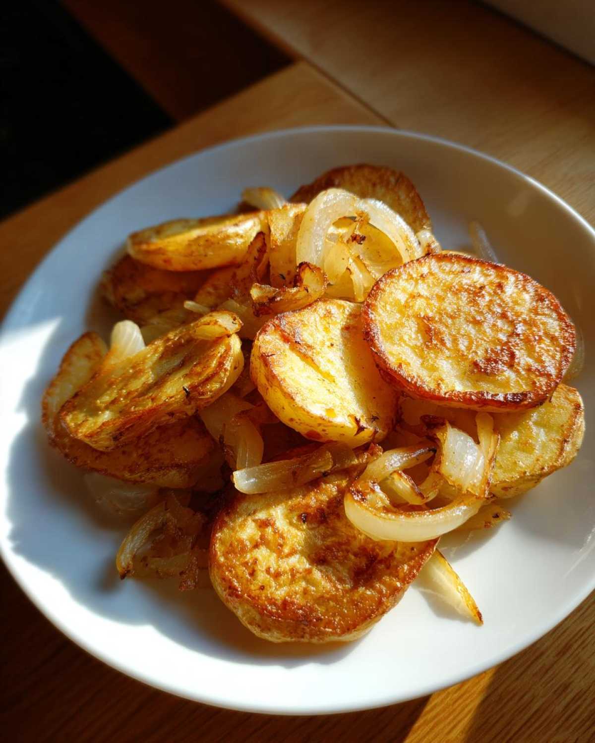 Golden brown, crispy fried potatoes served on a white plate mixed with sautéed onion slices.