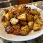 A white bowl filled with golden brown, crispy oven roasted potatoes seasoned with rosemary and pepper.
