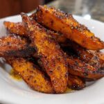 Close-up of perfectly crispy, seasoned sweet potatoes wedges piled high in a white bowl.
