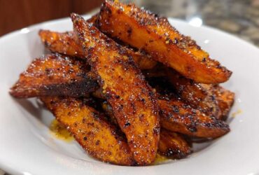Close-up of perfectly crispy, seasoned sweet potatoes wedges piled high in a white bowl.