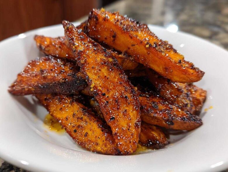 Close-up of perfectly crispy, seasoned sweet potatoes wedges piled high in a white bowl.