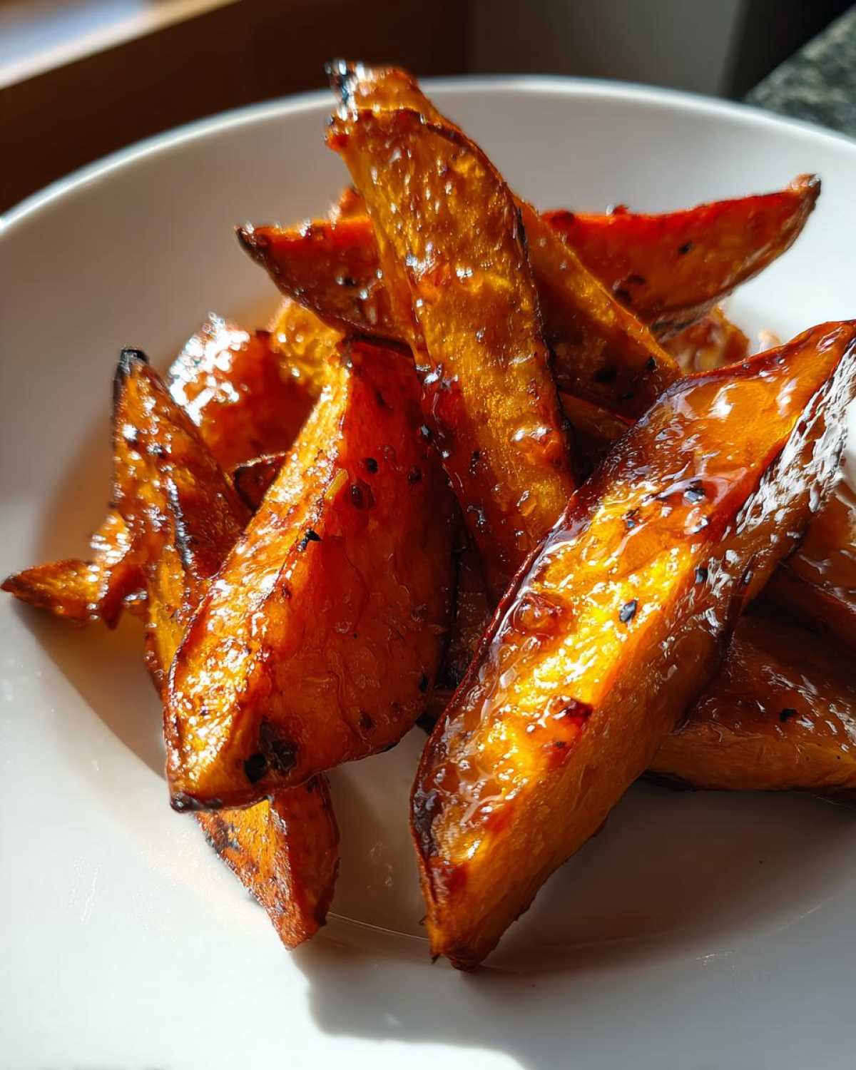 Close-up of perfectly caramelized and crispy sweet potatoes wedges piled in a white bowl.