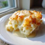 A generous serving of creamy crockpot cheesy potatoes topped with melted, browned cheese on a white plate.