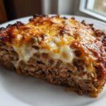 A thick slice of crockpot french onion meatloaf topped with melted, browned cheese on a white plate.