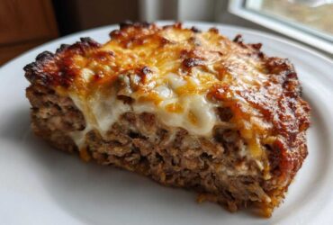 A thick slice of crockpot french onion meatloaf topped with melted, browned cheese on a white plate.