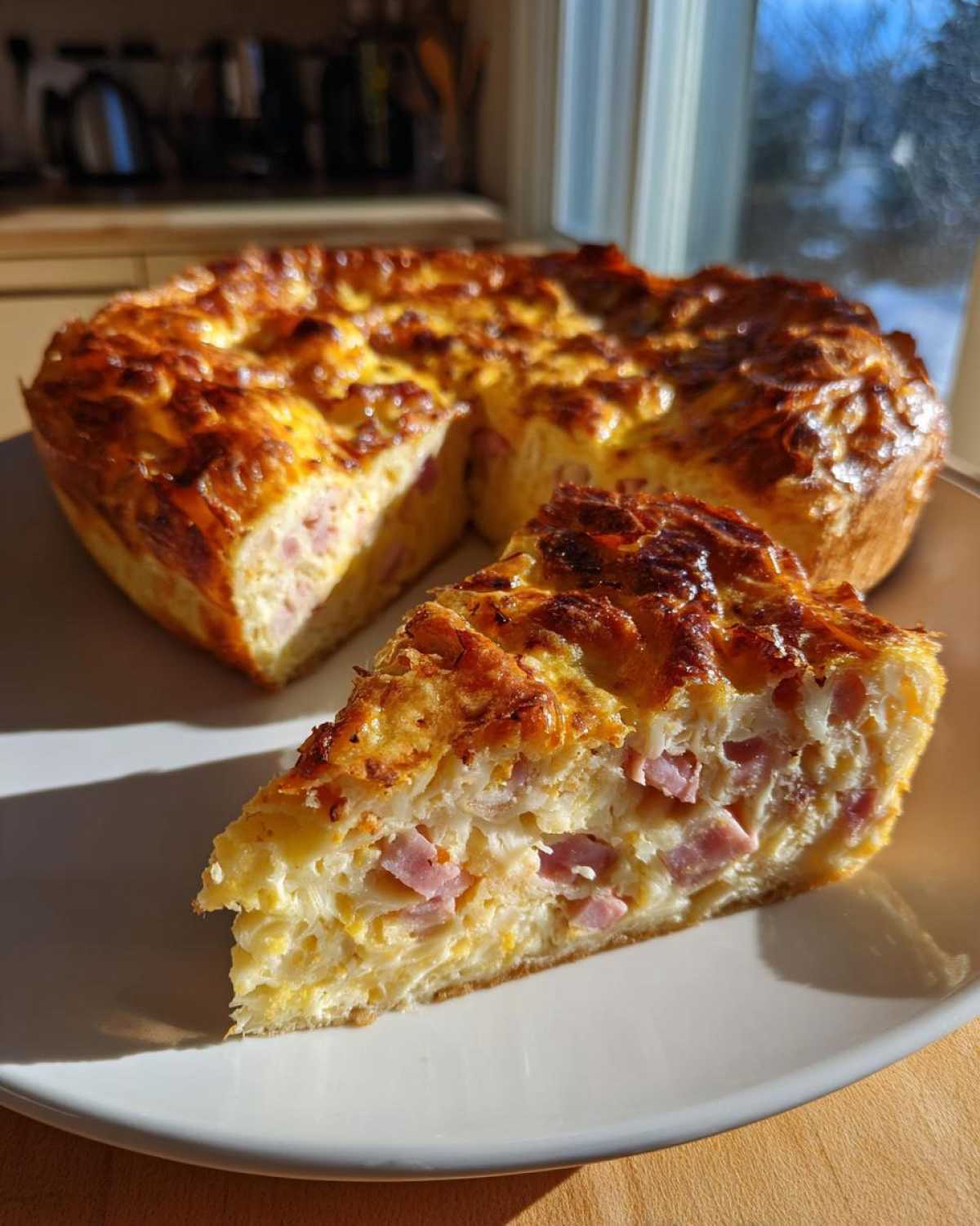 A slice of golden-brown Croissant Breakfast Casserole featuring visible pieces of ham, served on a white plate.