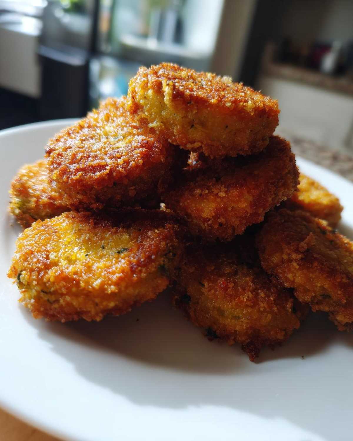 A close-up stack of golden brown, crispy Delicious Air Fryer Fried Pickles piled on a white plate.