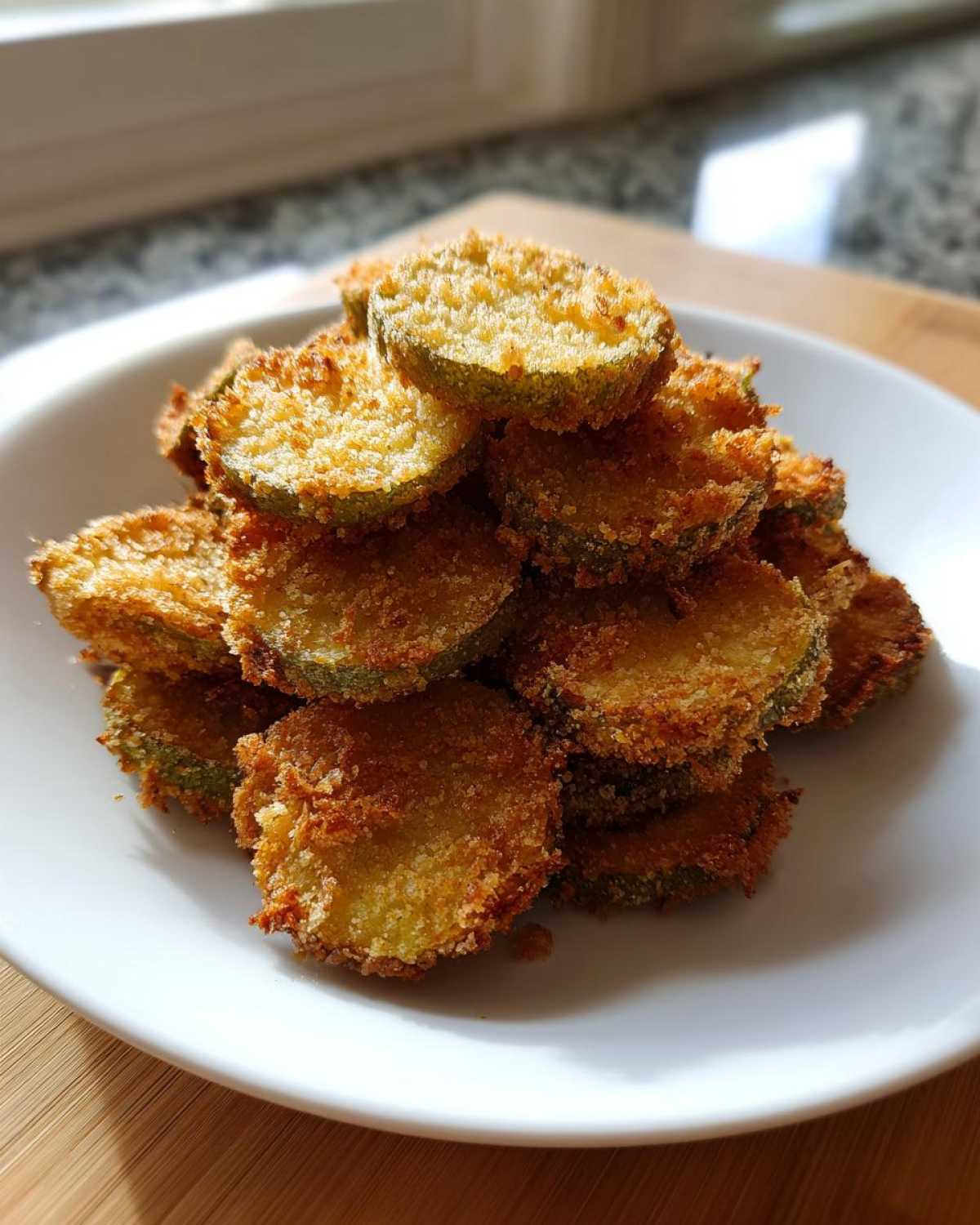 A white plate piled high with golden brown, crispy Delicious Air Fryer Fried Pickles slices.