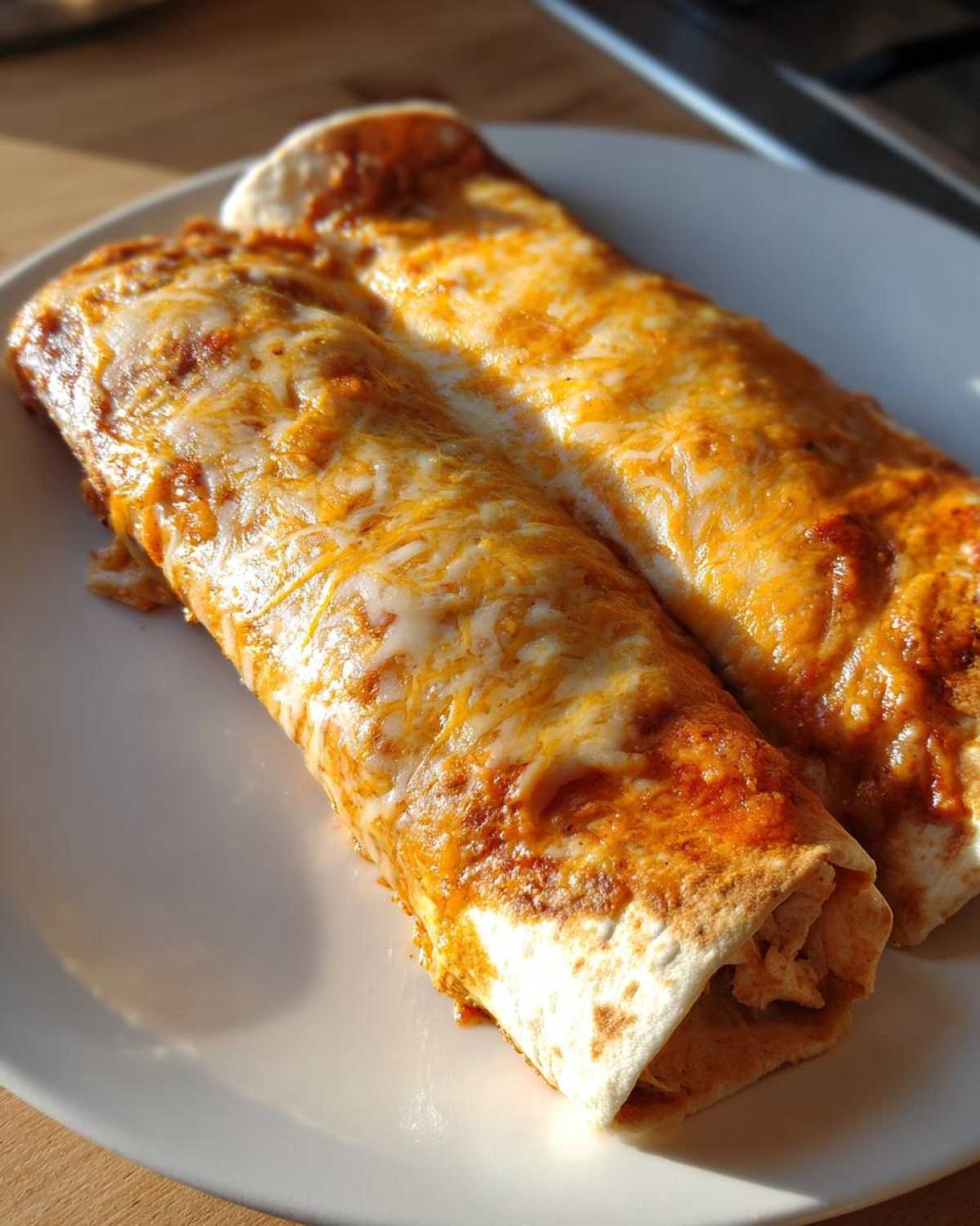 Close-up of two easy chicken enchiladas covered in melted orange and white cheese sauce on a white plate.