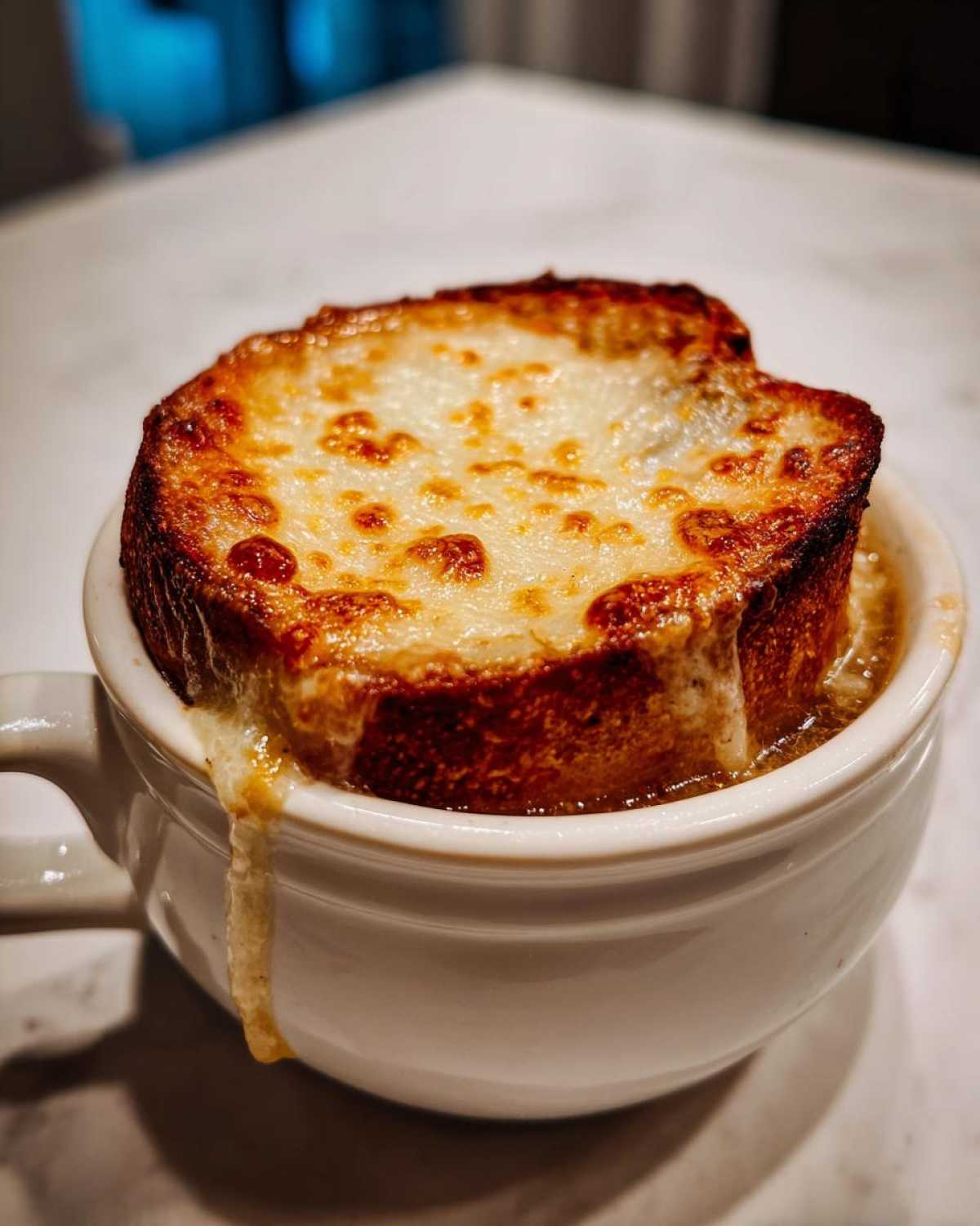 Close-up of a bowl of french onion soup topped with a thick, melted, and browned layer of cheese over crouton.