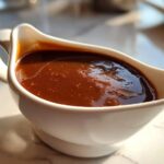 Close-up of rich, glossy homemade brown gravy served in a white ceramic gravy boat.