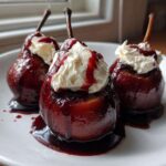 Three ruby-red poached pears topped with whipped cream and syrup, served on a white plate.