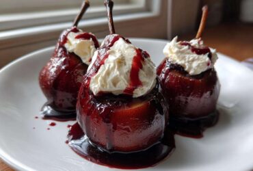 Three ruby-red poached pears topped with whipped cream and syrup, served on a white plate.