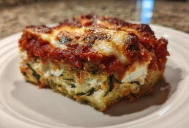 A close-up of a hearty slice of zucchini lasagna showing layers of ricotta, zucchini, and bubbling tomato sauce.